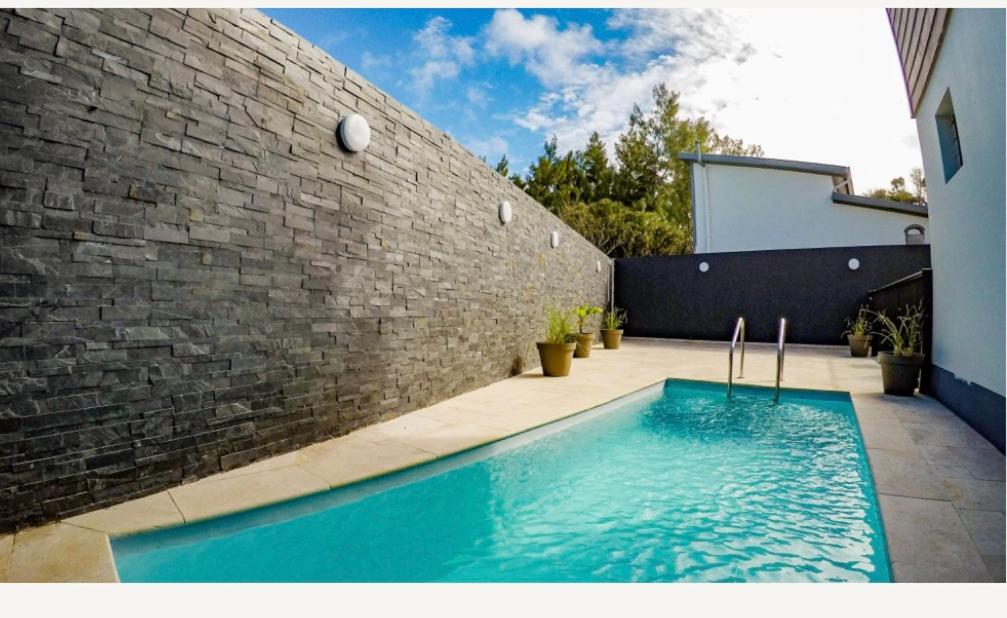 - une piscine en face d'un mur de briques dans l'établissement Les villas du cap piscine chauffée avril à octobre, à Saint-Joseph