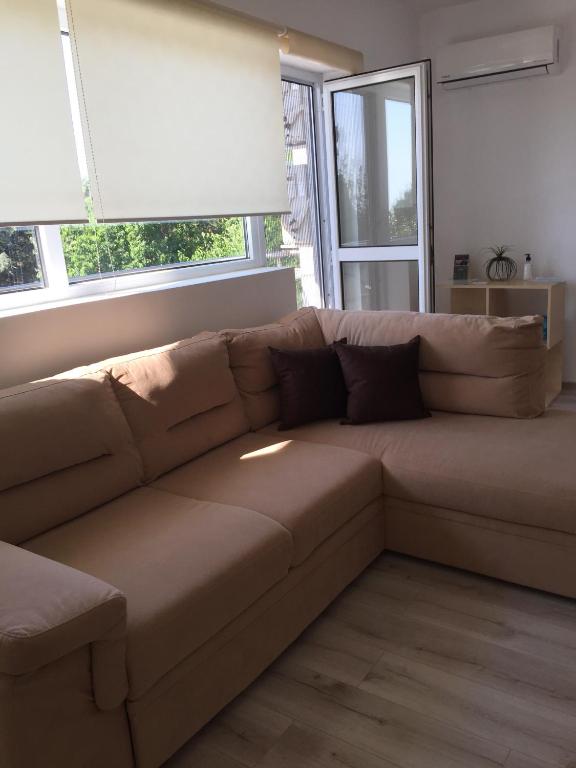 a brown couch in a living room with windows at Апартамент Евксиновград, една спалня - безплатен паркинг, Варна in Varna City