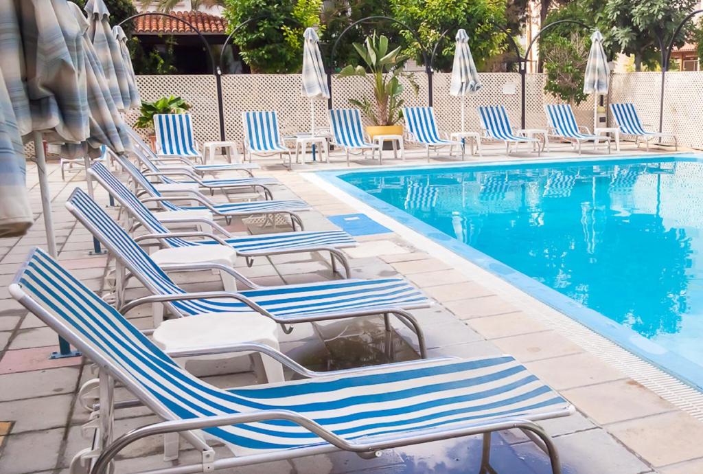 a row of lounge chairs next to a swimming pool at San Remo Hotel in Larnaca