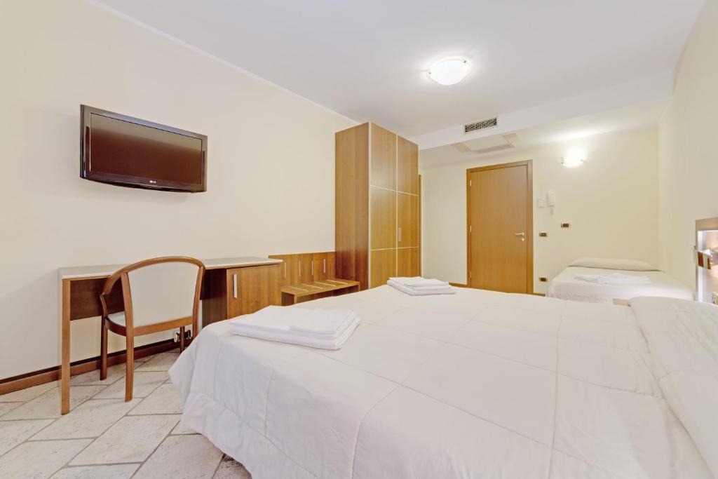 a bedroom with a large white bed and a desk at Hotel Grotto Bagat in Lavena Ponte Tresa