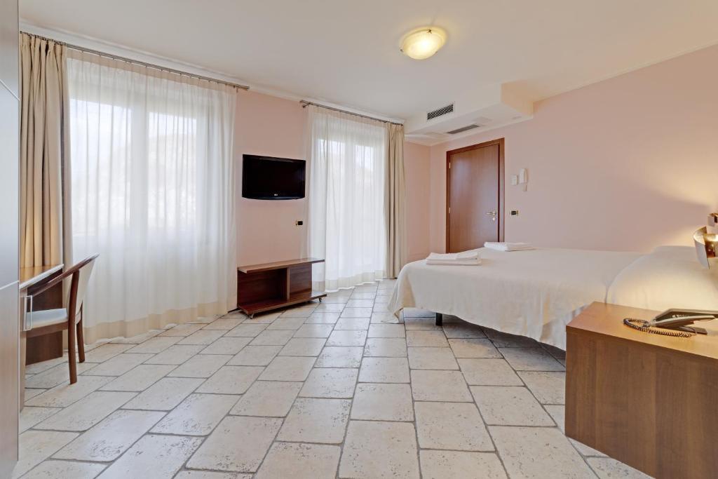 a bedroom with a bed and a desk and a tv at Hotel Grotto Bagat in Lavena Ponte Tresa