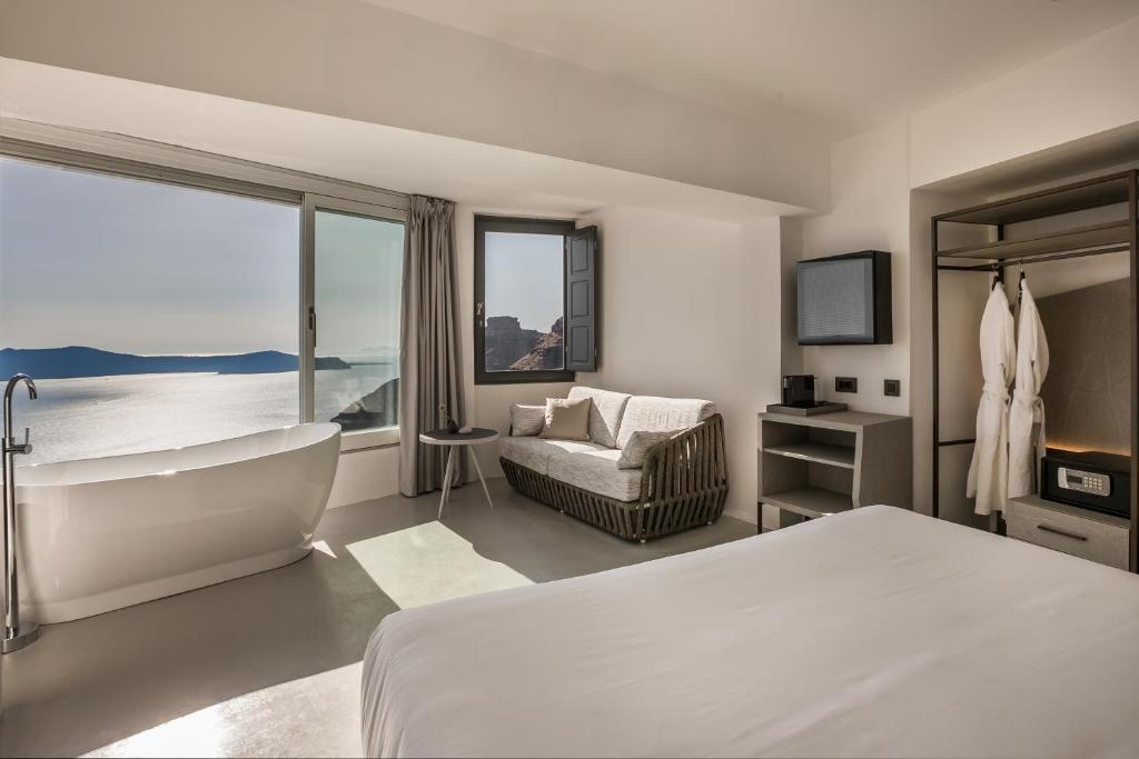 a bedroom with a tub and a bed and a television at Sun Rocks Boutique Hotel in Firostefani