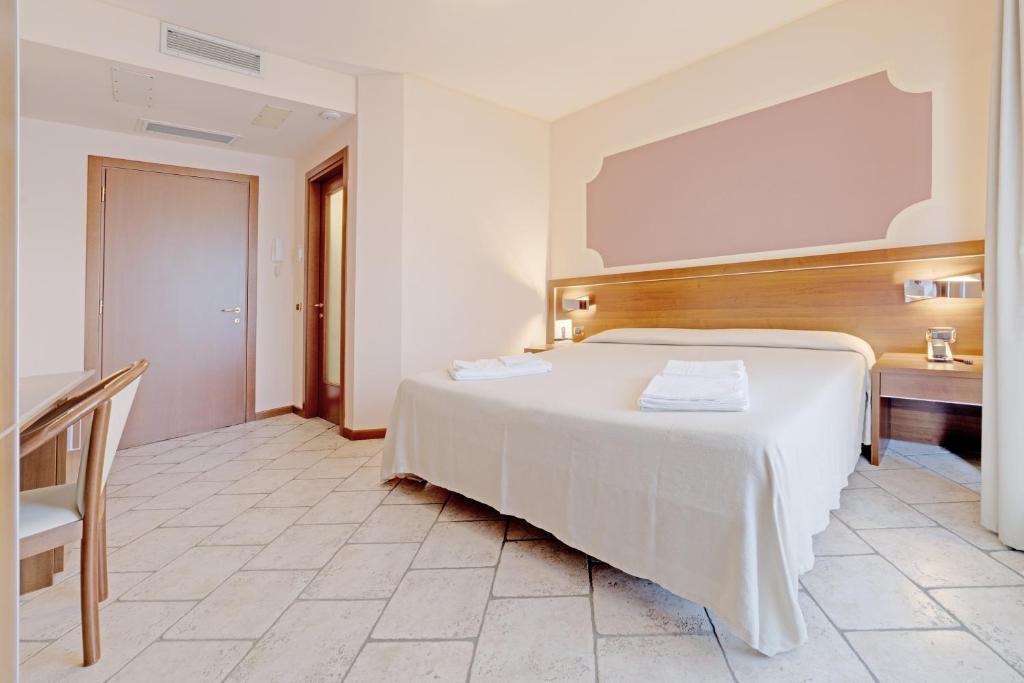a bedroom with a large white bed and a desk at Hotel Grotto Bagat in Lavena Ponte Tresa