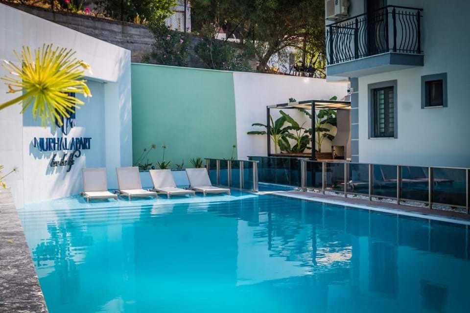 a pool with chairs and a building at Nurhal Apart in Muğla