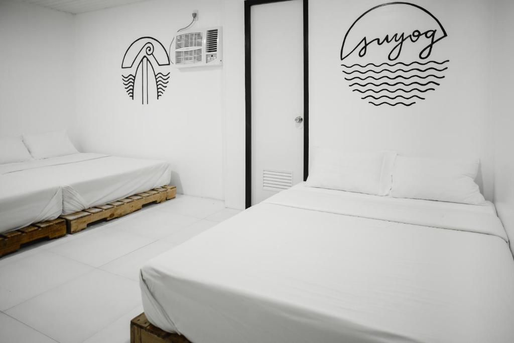 a white bedroom with two beds and a sign on the wall at Suyog Life Siargao in General Luna