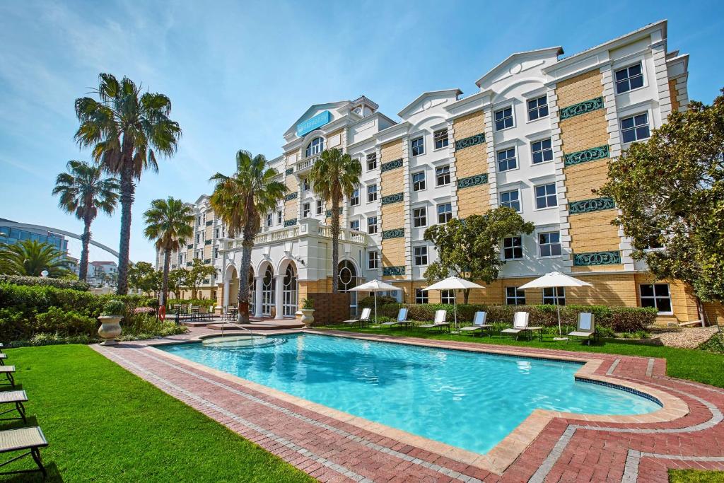 une piscine en face d'un bâtiment avec des palmiers dans l'établissement StayEasy Century City, au Cap