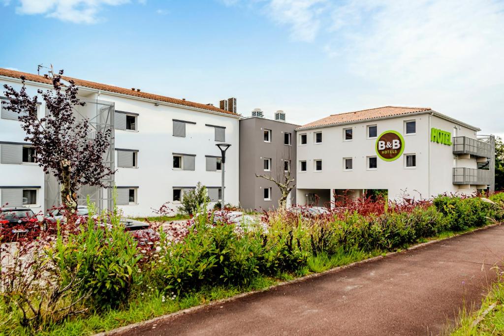 un bâtiment blanc avec un panneau sur le côté d'une route dans l'établissement B&B HOTEL Bordeaux Le Haillan, au Haillan