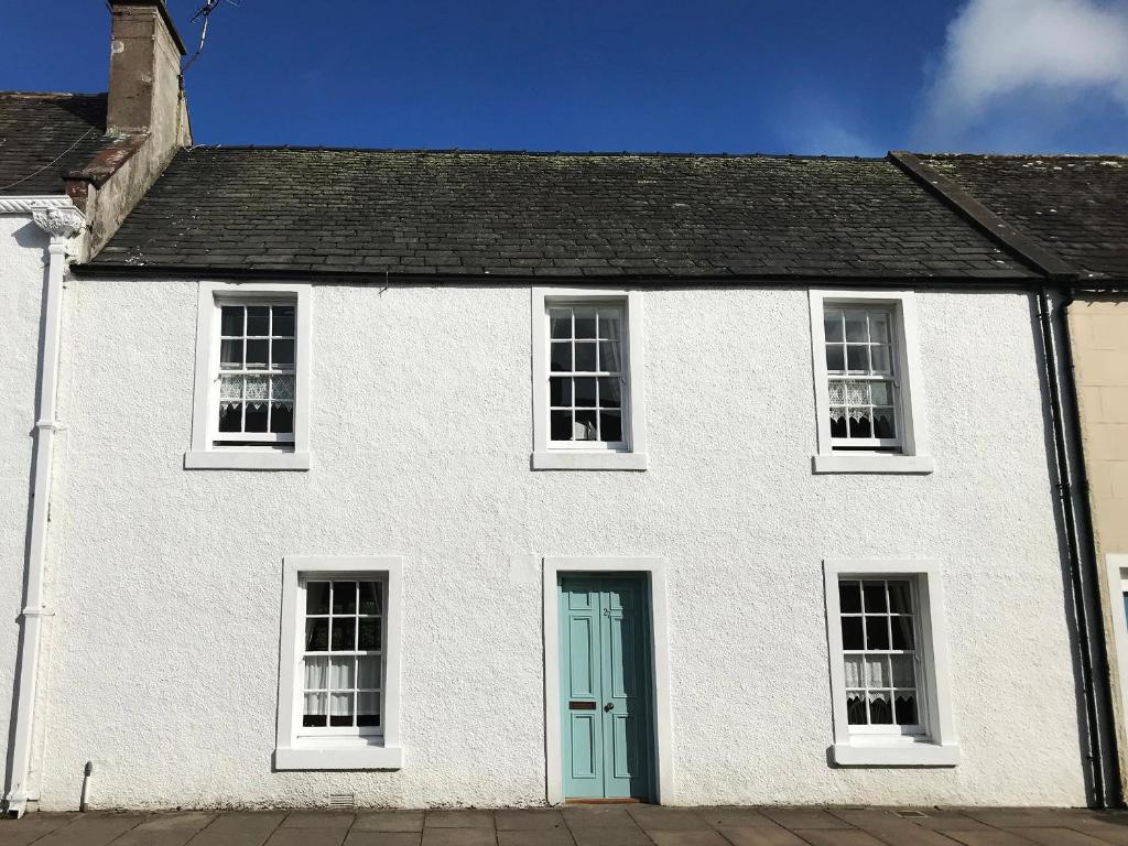 a white house with a blue door at Dermot Cottage in Gatehouse of Fleet