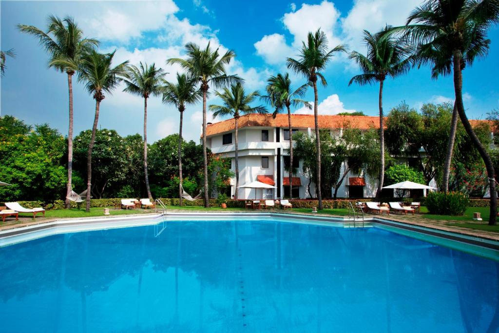 a swimming pool in front of a hotel with palm trees at Trident Chennai in Chennai