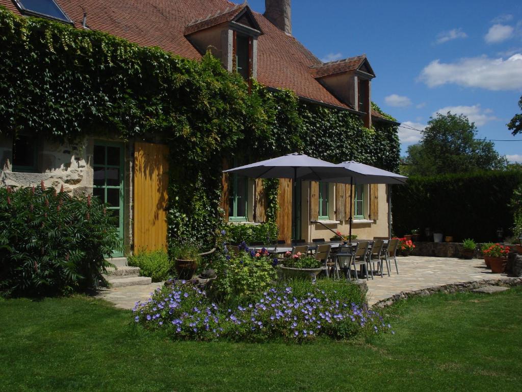 a house with an umbrella and chairs and flowers at La Maison du Cerf in Urciers