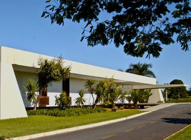 a white building with palm trees in front of a street at Centro de Brasília, 5 minutos da Esplanada dos Ministérios in Brasilia