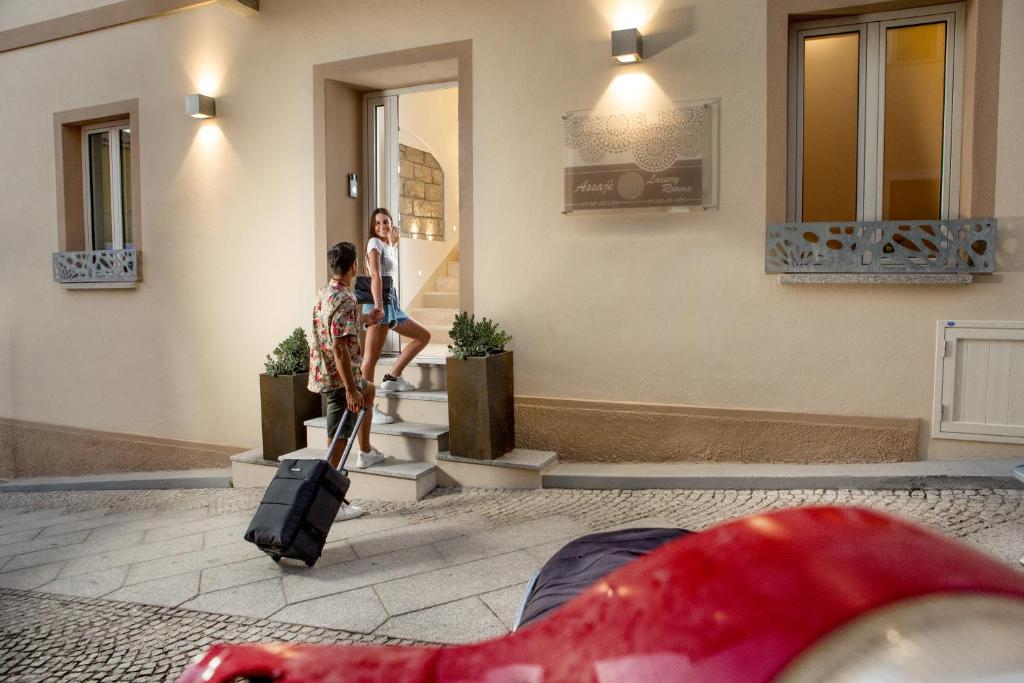 2 personnes marchant devant un bâtiment avec leurs bagages dans l'établissement Assaje' Luxury Rooms, à Santa Teresa Gallura