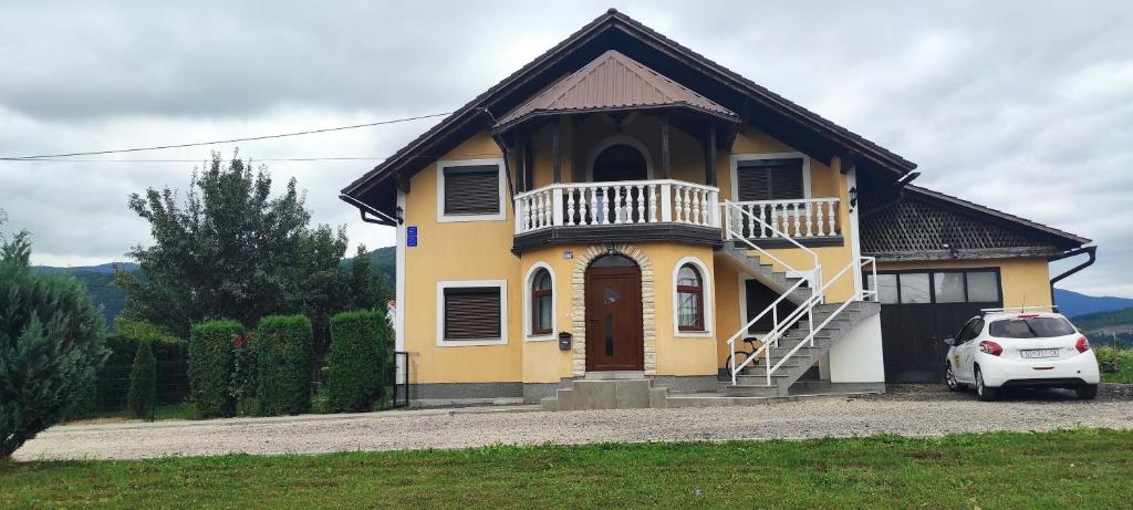una casa amarilla con un coche blanco aparcado delante en Apartman Majetić en Otočac