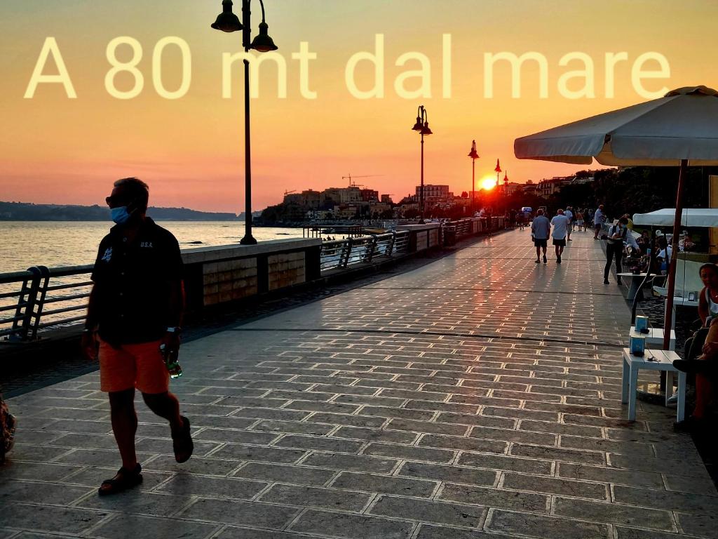 a man wearing a face mask walking on a pier at sunset at Pozzuoli 100per100 Home in Pozzuoli