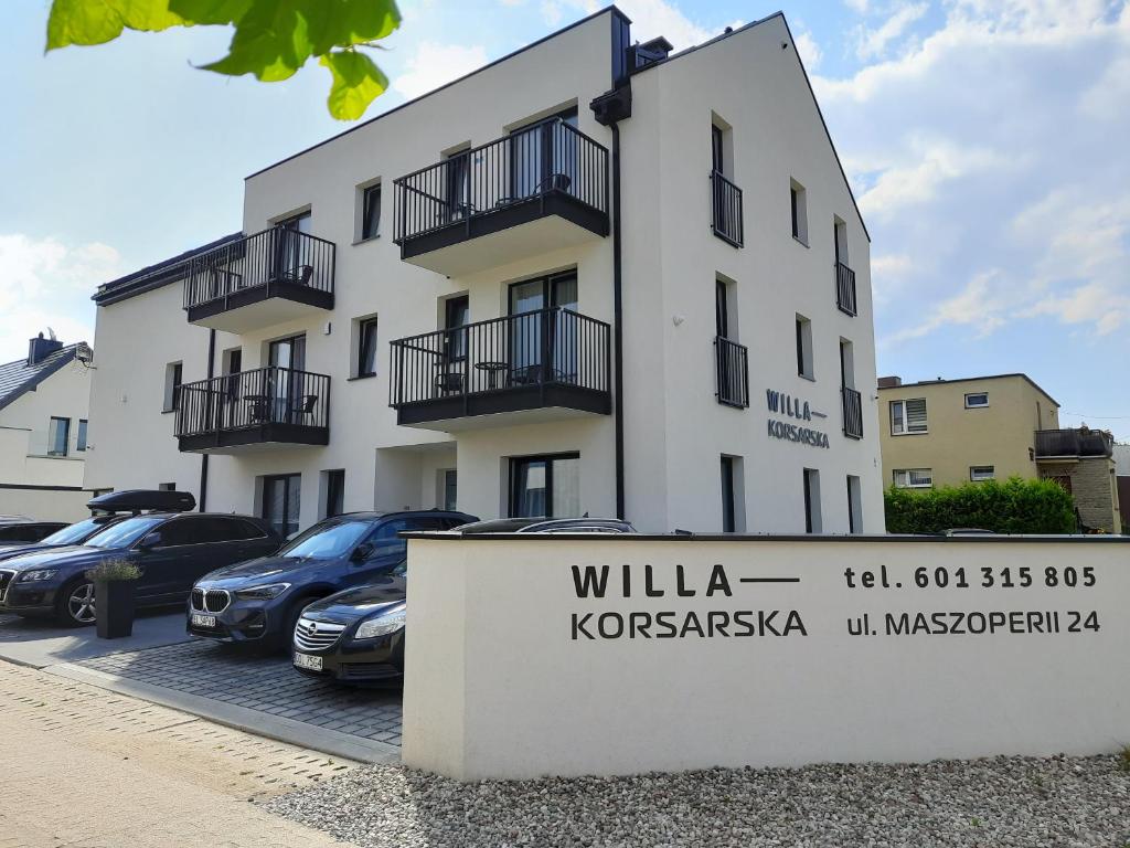 een wit gebouw met auto's geparkeerd op een parkeerplaats bij WILLA KORSARSKA in Władysławowo
