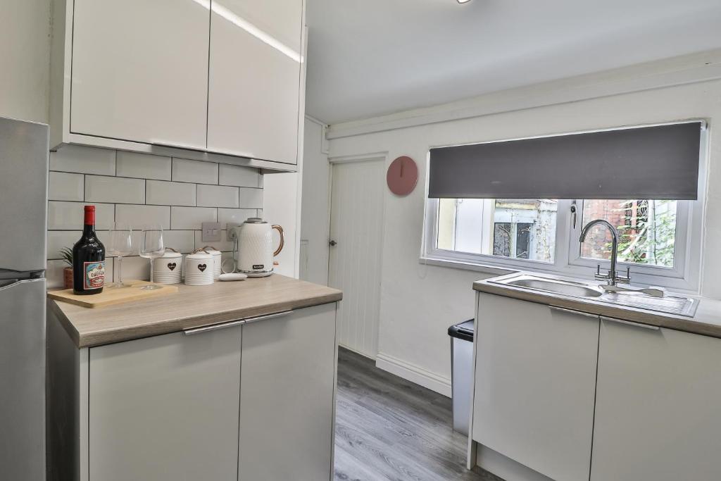 a kitchen with white cabinets and a sink and a window at Cozy Cribs near Zipworld, Dare Valley Bike Park, Pen-y-fan & Four Waterfalls Walk in Aberdare