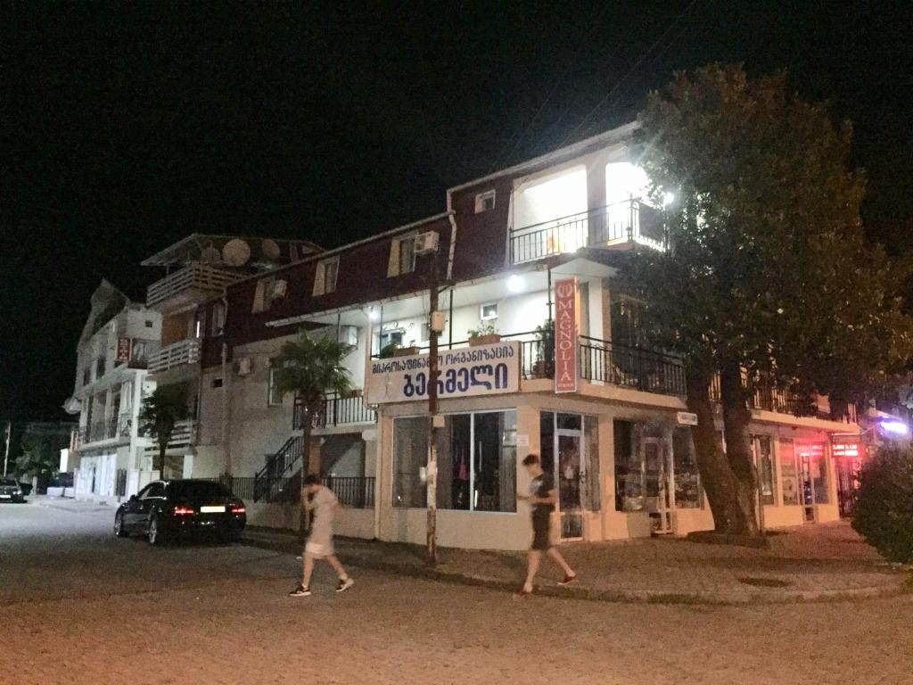 dos personas caminando en frente de un edificio por la noche en Magnolia Guest House, en Kobuleti