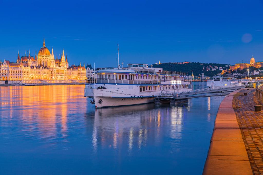 a large white boat in the water in front of a building at Grand Jules - Boat Hotel in Budapest
