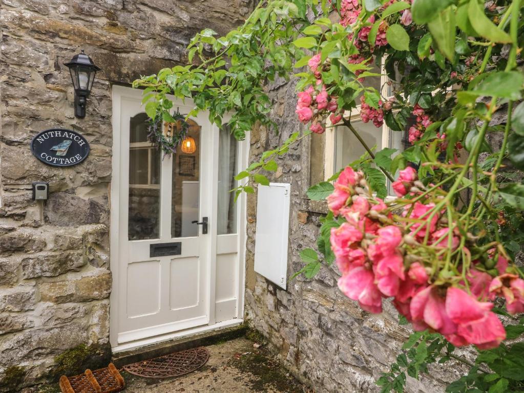 a stone house with a white door and pink flowers at Nuthatch Cottage in Skipton