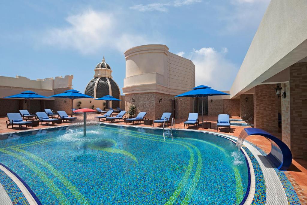 ein Pool auf dem Dach eines Hotels mit Stühlen und Sonnenschirmen in der Unterkunft Royal Rose Abu Dhabi in Abu Dhabi