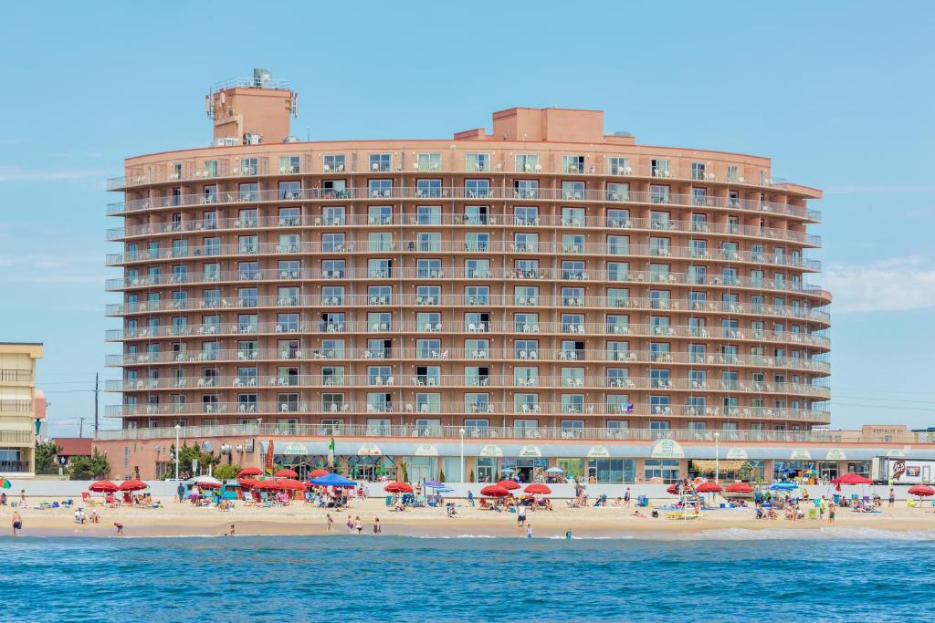 Grand Hotel Ocean City Oceanfront في آوشين سيتي: مبنى كبير على الشاطئ مع شاطئ به مظلات