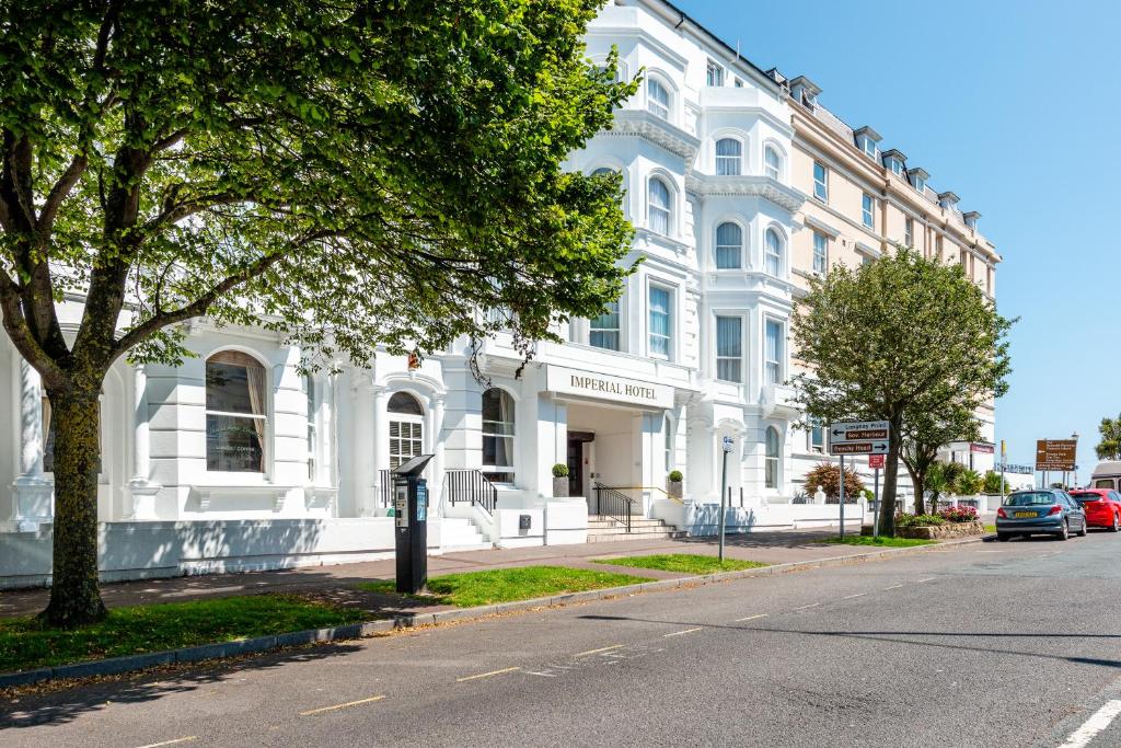 a large white building on a street with a tree at Imperial Hotel in Eastbourne