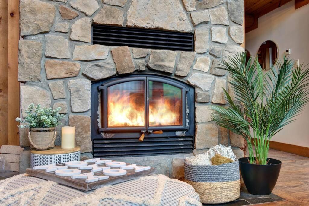 a stone fireplace with a table in front of it at LOG CABIN w HOT TUB, BEACH access, near of TREMBLANT in Labelle