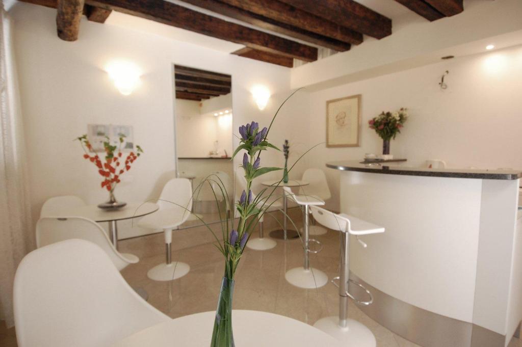 ヴェネツィアにあるサンタ マルゲリータ ゲスト ハウスの白い椅子と花瓶がテーブルに飾られた部屋