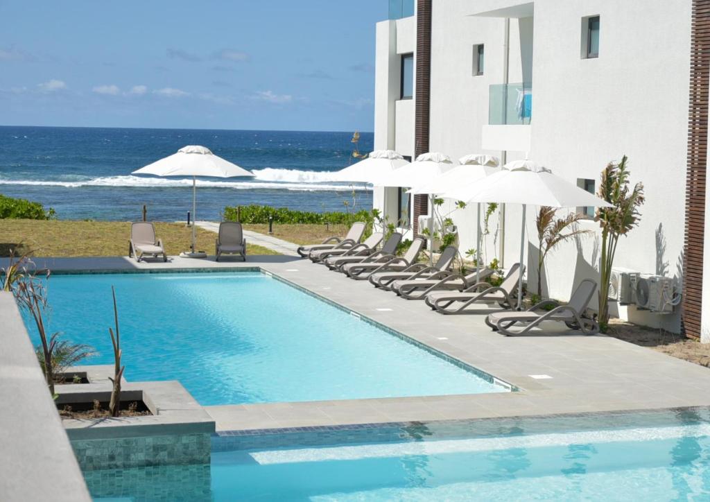 a swimming pool with chairs and umbrellas and the ocean at Eastern Blue - Sea View Luxury Apartment in Poste Lafayette