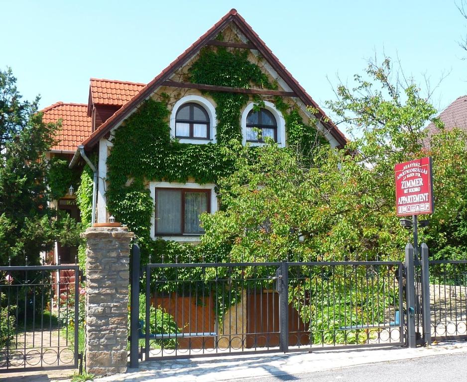 una casa cubierta de hiedra con una valla y una señal en Aranyház Apartmanszállás, en Tihany