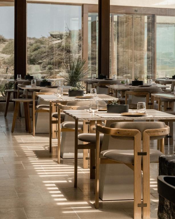 a restaurant with wooden tables and chairs and windows at Acro Suites - A Wellbeing Resort in Agia Pelagia