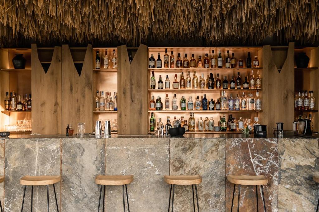 a bar with three stools in front of a wall of bottles at Acro Suites - A Wellbeing Resort in Agia Pelagia