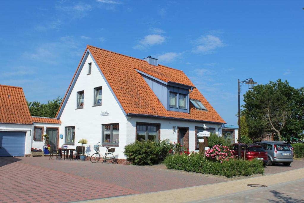 ein weißes Haus mit orangefarbenem Dach auf einer Straße in der Unterkunft Haus Anker in Neuharlingersiel