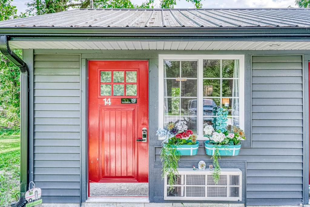 eine rote Tür in einem grauen Haus mit Blumen im Fenster in der Unterkunft Lighthouse Kitchen Suites near Auburn Waterloo I-69 Exit 334 in Auburn