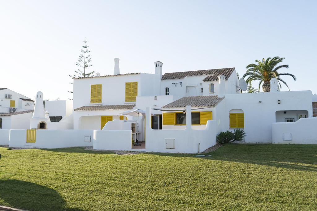 uma casa branca com persianas amarelas e um quintal em Hopstays Vilamoura Aldeia do Golfe - House C3 em Vilamoura