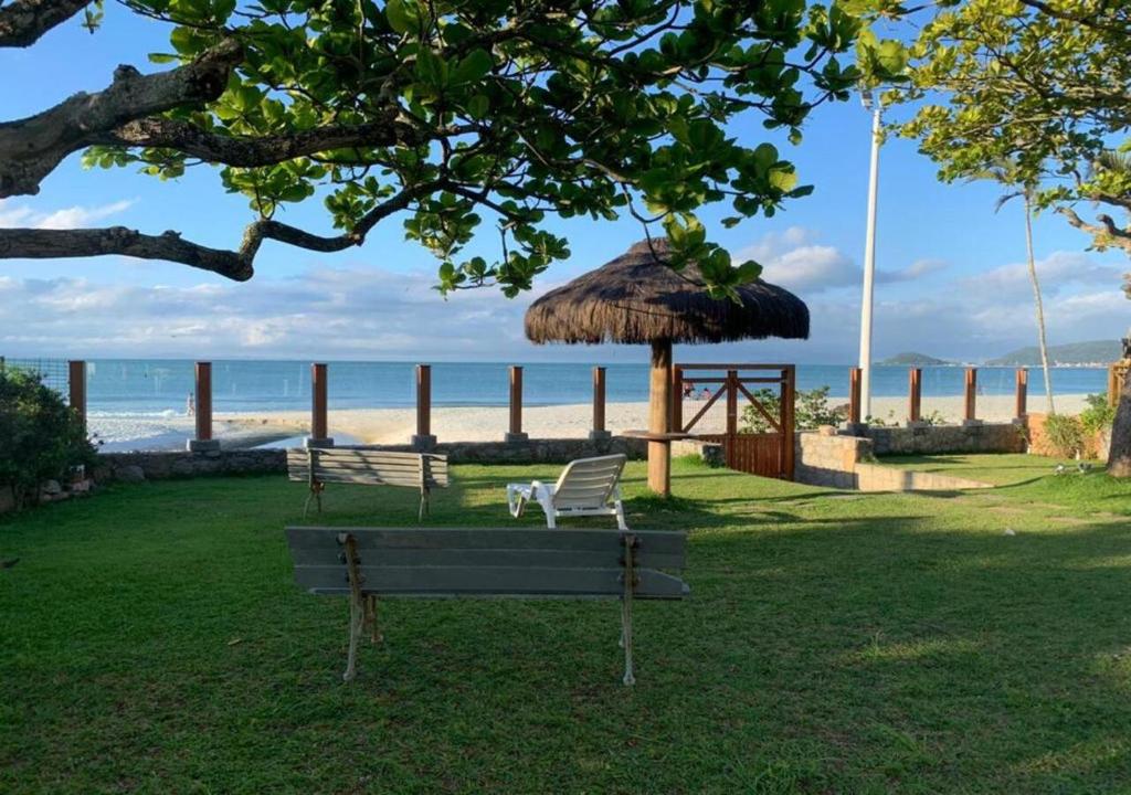 um banco de parque com um guarda-sol de palha e a praia em Light Beach Residence em Florianópolis