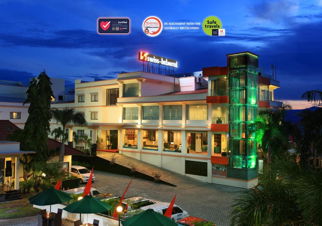 a hotel building with a neon sign in front of it at Swiss-Belhotel Silae Palu in Palu