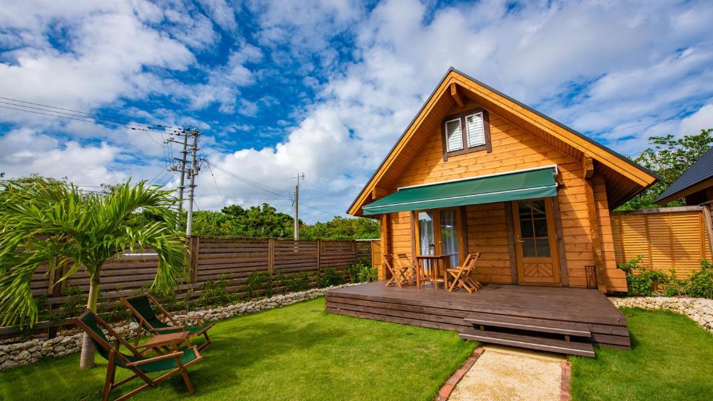 ein kleines Holzhaus mit einer Terrasse und Stühlen in der Unterkunft ロガシス石垣野底ヴィラ in Ibaruma