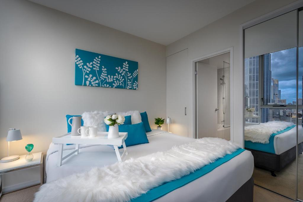 a white and blue bedroom with a bed and a table at Milano Serviced Apartments in Melbourne