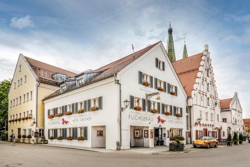 un grand bâtiment blanc dans une rue avec une église dans l'établissement Fuchsbräu, à Beilngries