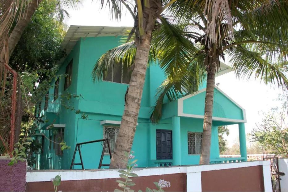 a blue house with palm trees in front of it at Satya Vacation Stay in Alibaug