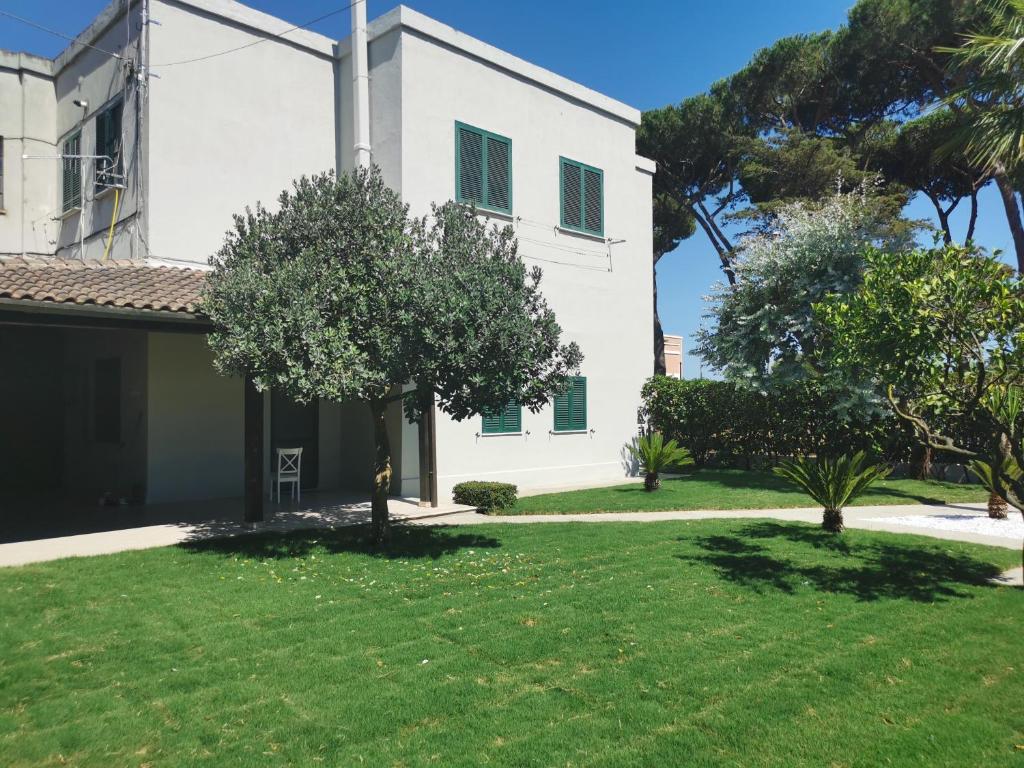 a white house with a green yard with trees at La Rosa Casa Vacanze Sabaudia in Sabaudia