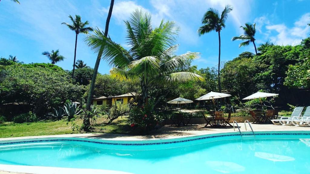 a pool with palm trees and chairs and umbrellas at Pousada Araçás Village in Imbassai