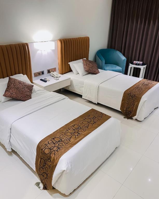 a hotel room with three beds and a blue chair at White Orchid in Cox's Bazar