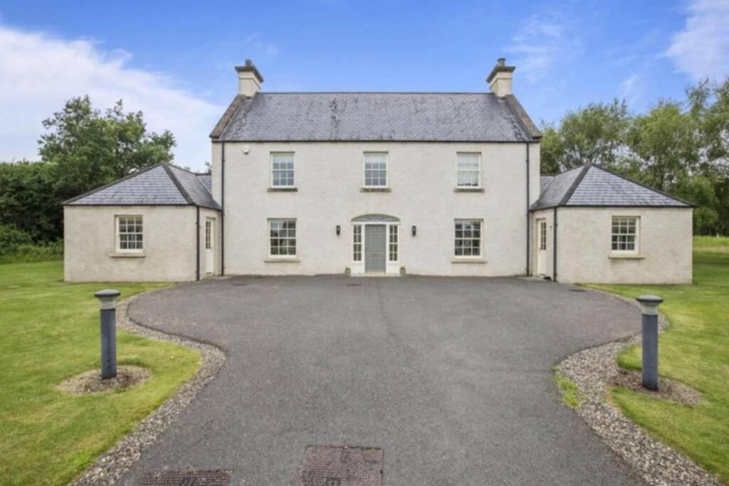 uma grande casa branca com uma entrada em The Lough Erne House at Golf Village Lough Erne Resort em Enniskillen