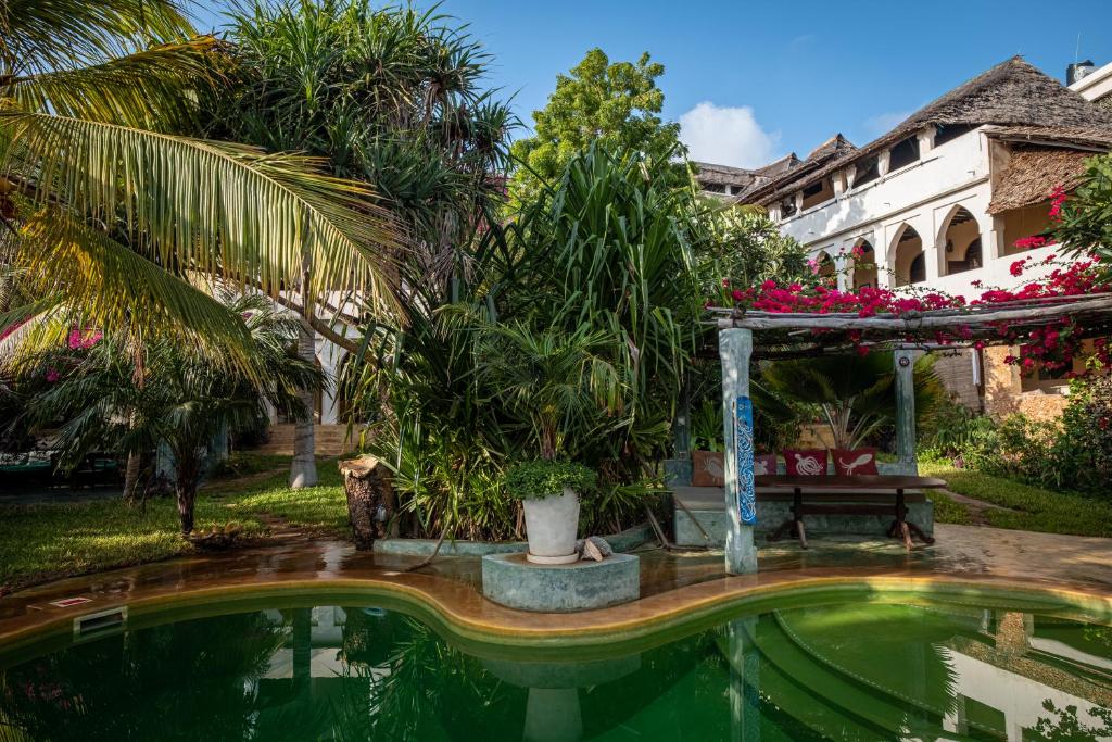 a pool in a garden with a bench and a building at Banana House and Wellness Centre in Lamu