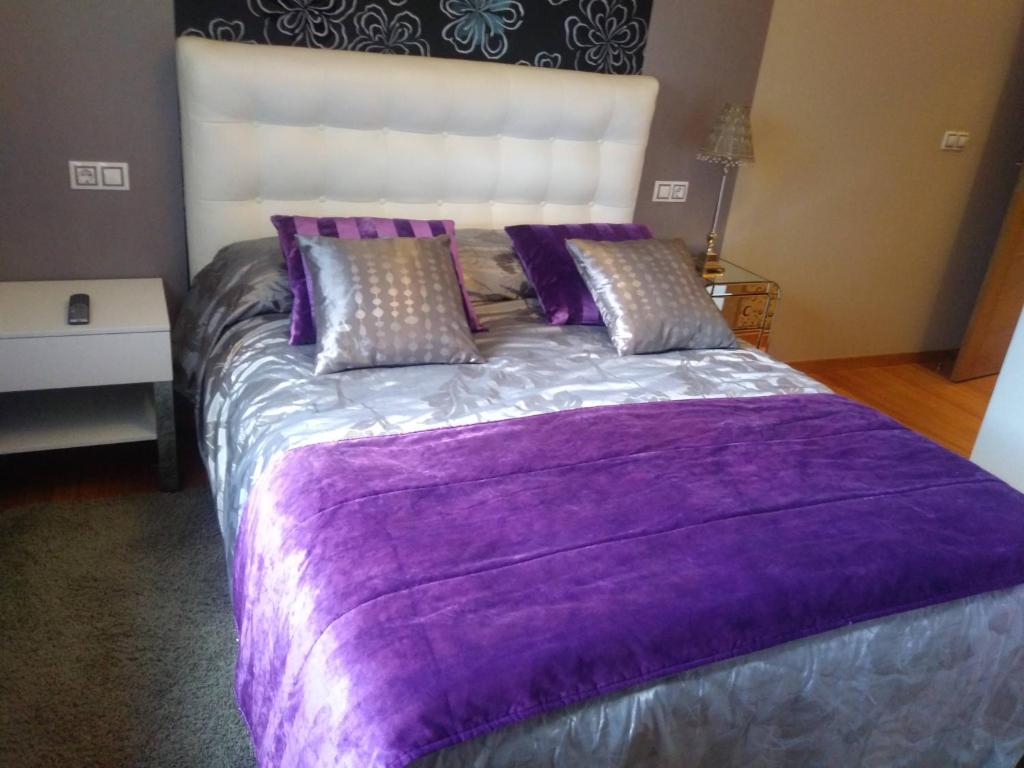Cama grande con manta y almohadas moradas en Apartamento Las Carolinas, en Ribeira