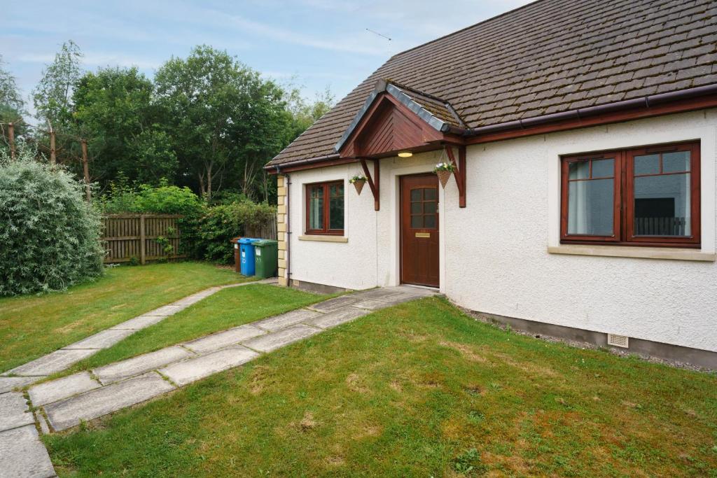 a small white house with a yard with a driveway at The Nook Holiday Cottage in Aviemore