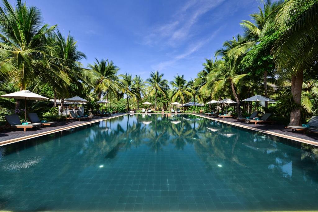 a large swimming pool with palm trees and umbrellas at Royal River Kwai Resort and Spa -SHA Extra Plus in Kanchanaburi