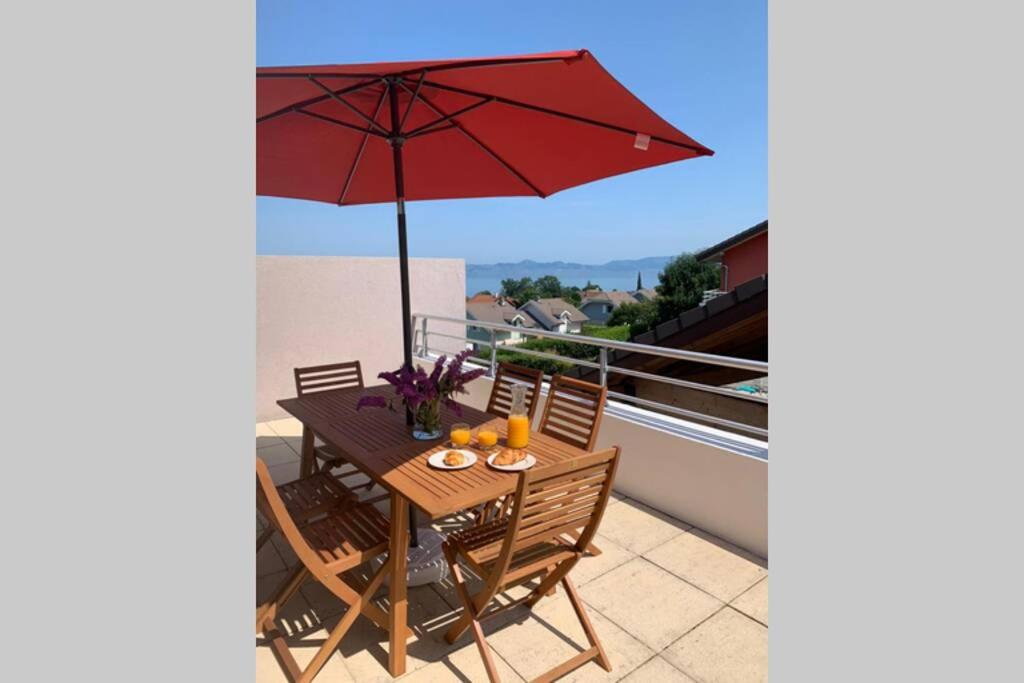 una mesa de patio con una sombrilla roja en el balcón en Superbe appartement au calme avec vue sur le Lac. en Évian-les-Bains